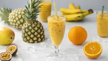 Tropisk smoothie i et glass med friske frukter som mango og ananas, servert på en kjøkkenbenk.