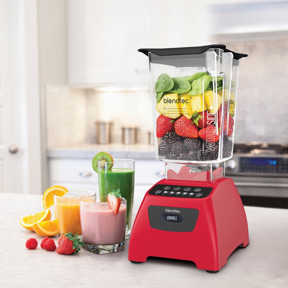 Rød Blendtec Classic 575 blender fylt med friske bær, spinat og ananas på et kjøkken, med tre fargerike smoothies ved siden av.
2.plass beste blender til smoothie blender best i test