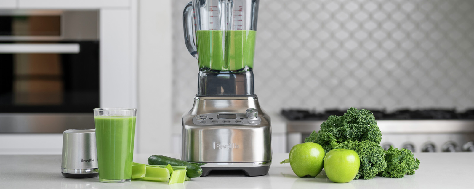 Breville Super Q Blender with fresh green smoothie, celery, cucumber, apples, and kale on a kitchen counter.