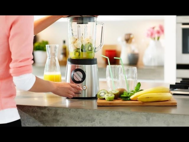 Problend 6 blender creating a fresh smoothie with pineapple, orange, and leafy greens on a countertop with fitness gear nearby.