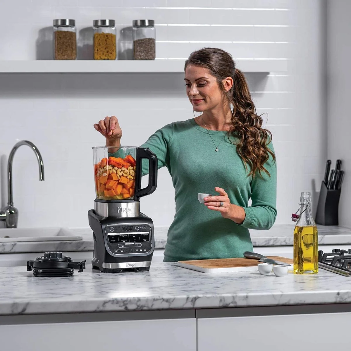 Woman using a Ninja hot and cold blender to prepare a healthy soup with vegetables and nuts in a modern kitchen.